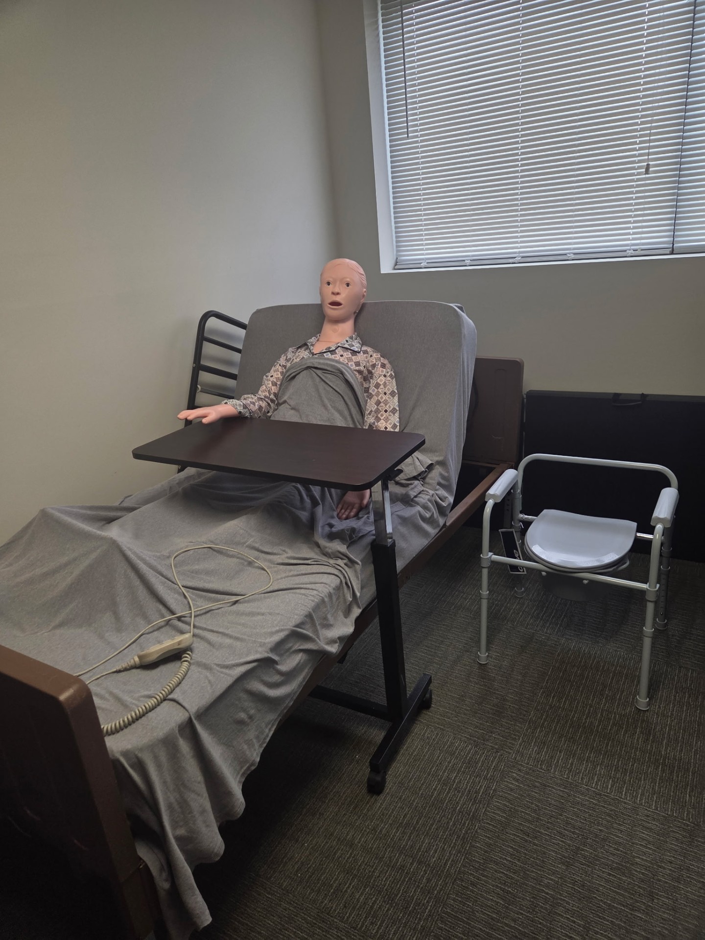 Caregiver training station with hospital bed, bedside commode, and mannequin